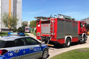 Służby ratunkowe na miejscu interwencji. Radiowóz policji i straży pożarnej oraz karetka pogotowia na osiedlu wśród bloków.