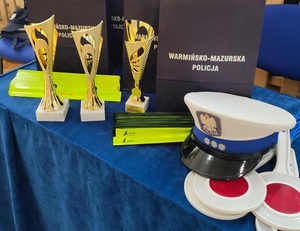 Puchary, torebki z napisem policja, tarcze STOP i czapka policjanta ruchu drogowego położone na stole