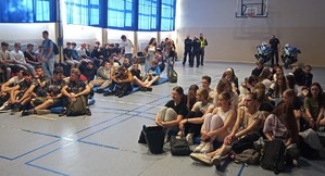 uczestnicy spotkania na sali gimnastycznej, w tle policjanci i motocykle policyjne